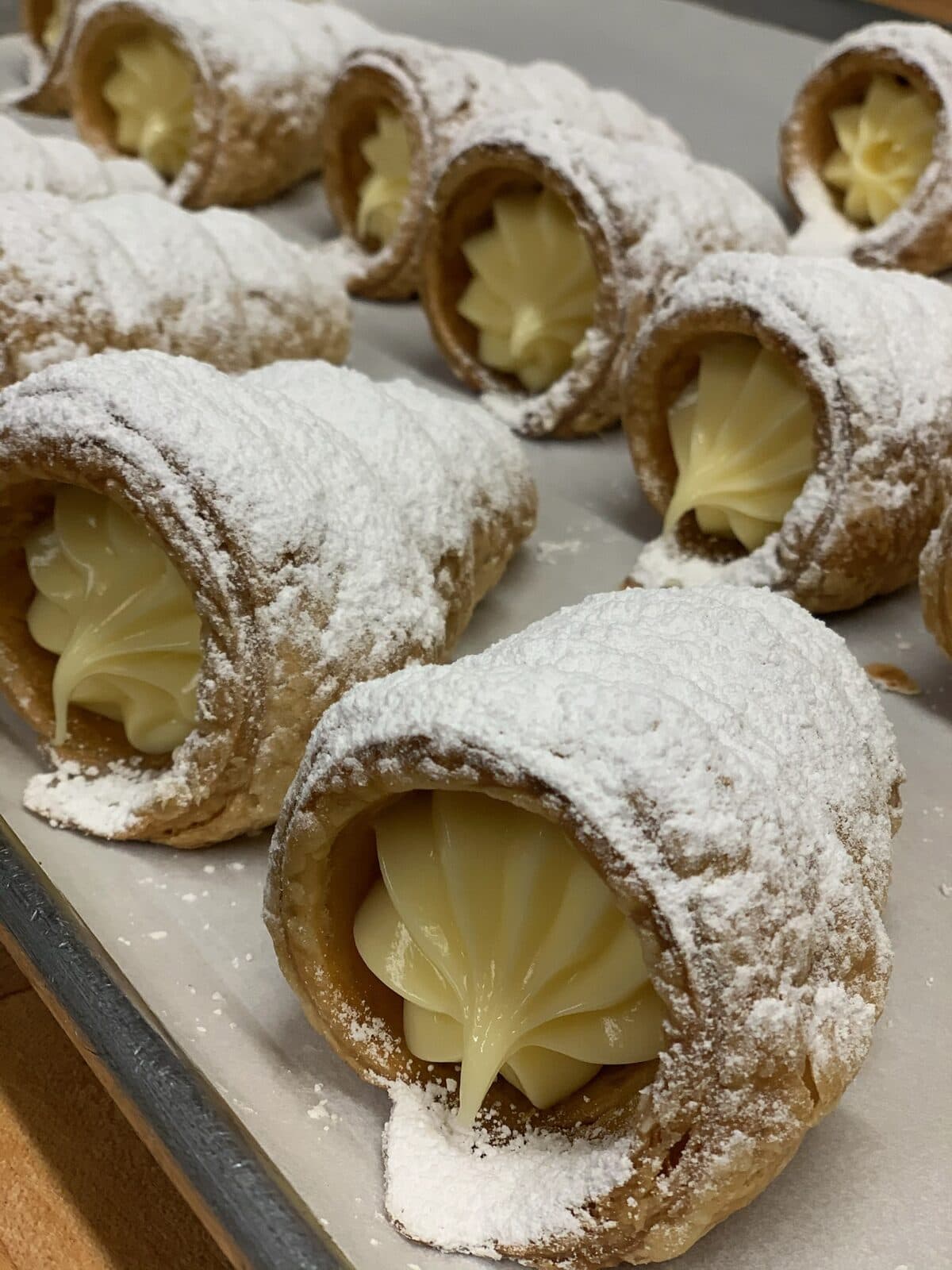 Filas de conos rellenos de crema espolvoreados con azúcar glass sobre una charola de hornear