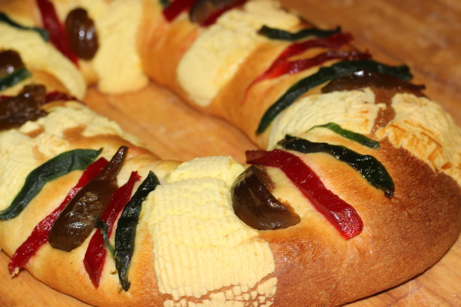 Primer plano de una Rosca de Reyes terminada con pasta de azúcar y fruta confitada sobre una mesa de madera